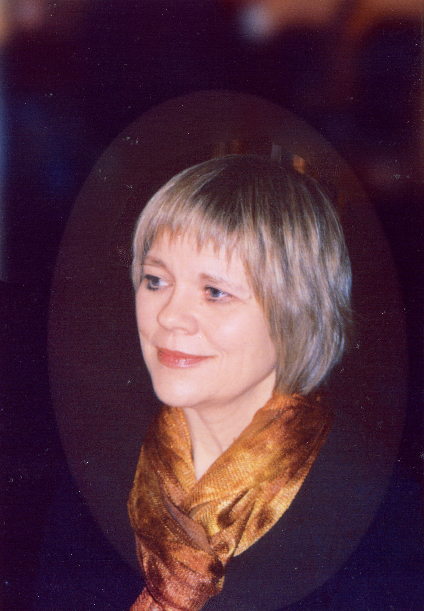 Photo of the author, Jannie Edwards. Against a black backdrop, she is wearing a black top and a golden scarf, and her blond hair sits at her shoulders.