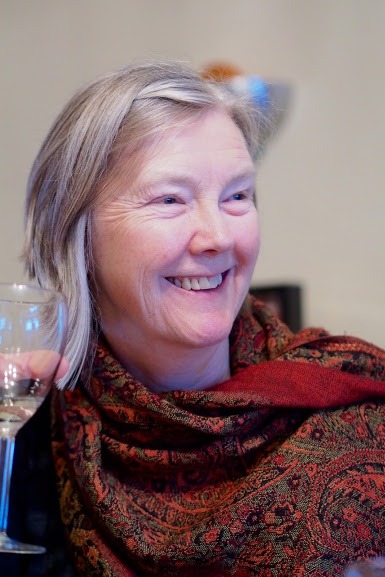 Photo of the author, Frances Boyle. She is smiling and wearing a red patterned scarf, and holding a glass of white wine.